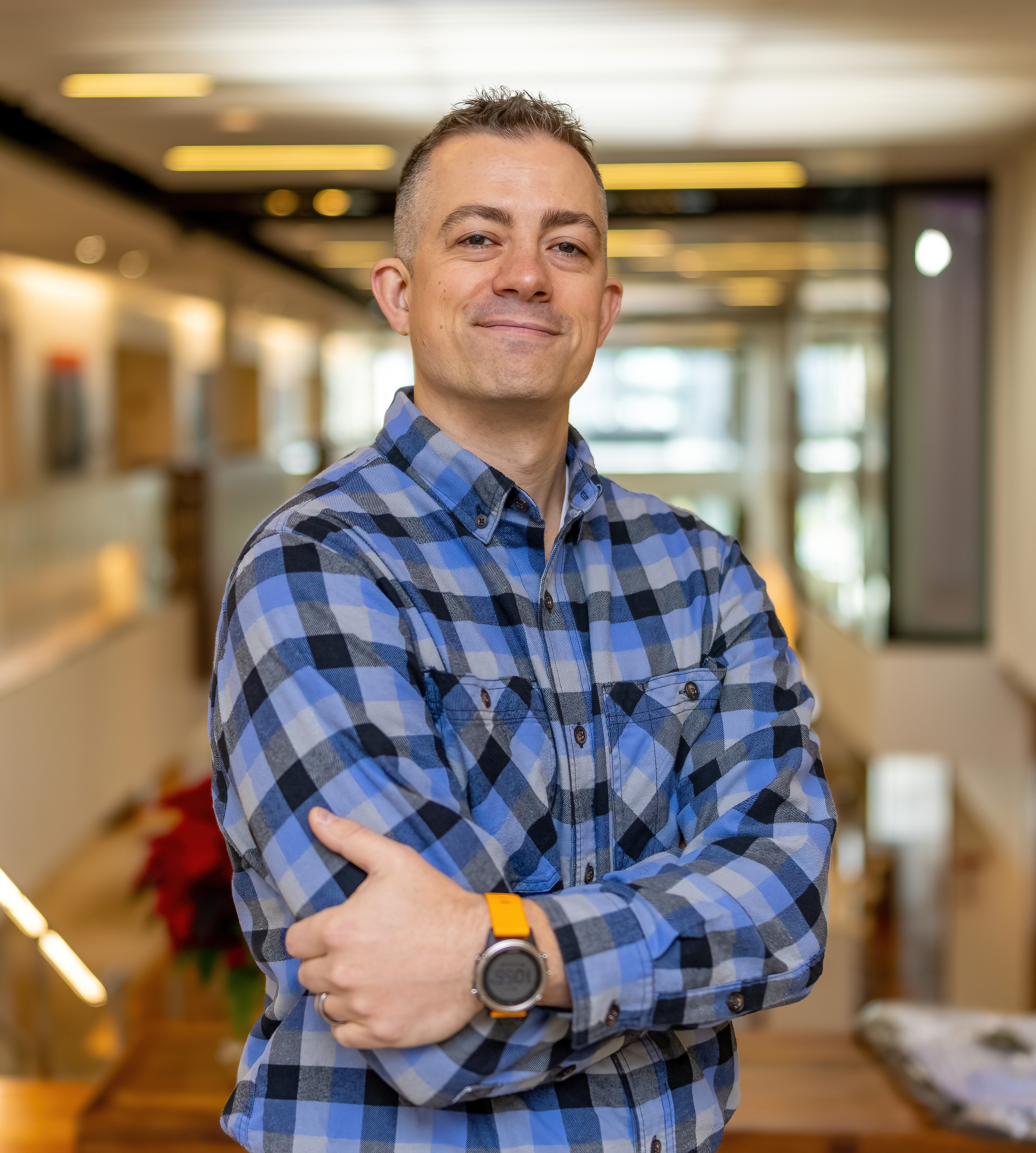 Dan stands, arms crossed, with a blue flannel shirt on, smiling at the camera.